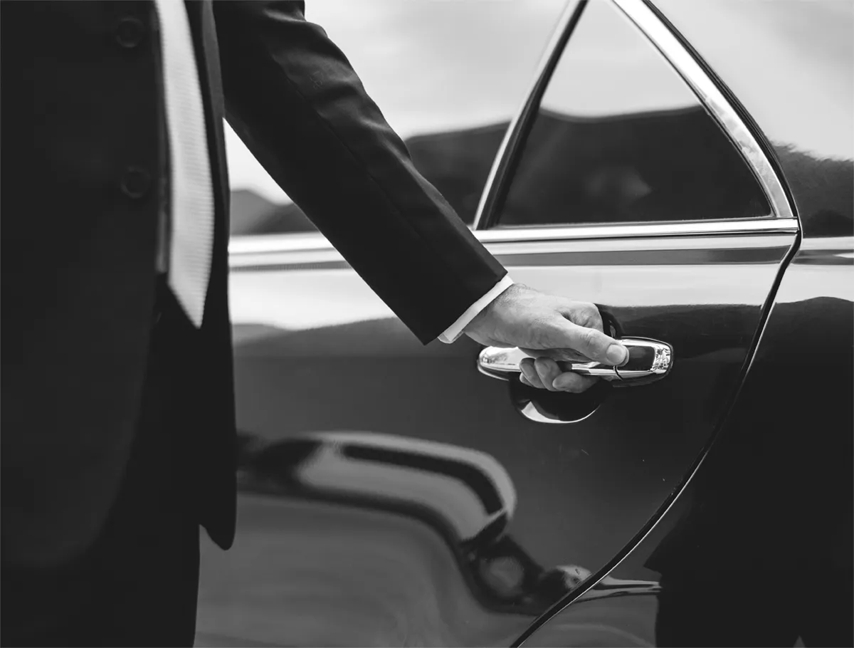 A chauffeur’s hand on the door handle of a polished black car