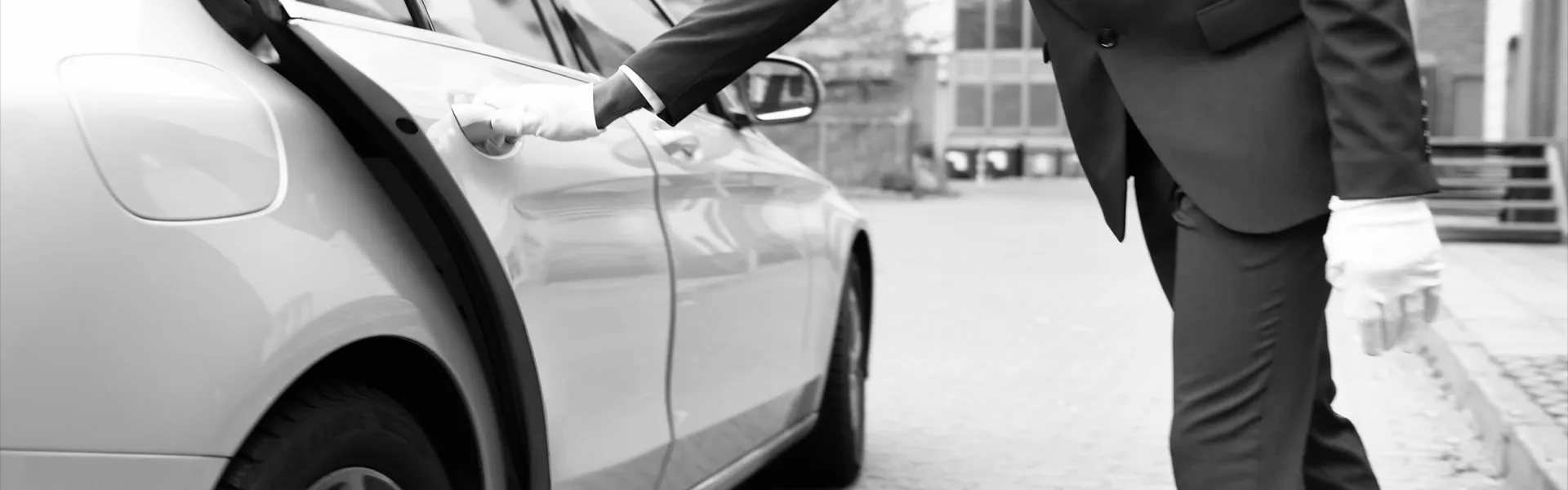 A chauffeur in white gloves opening the rear door of a saloon