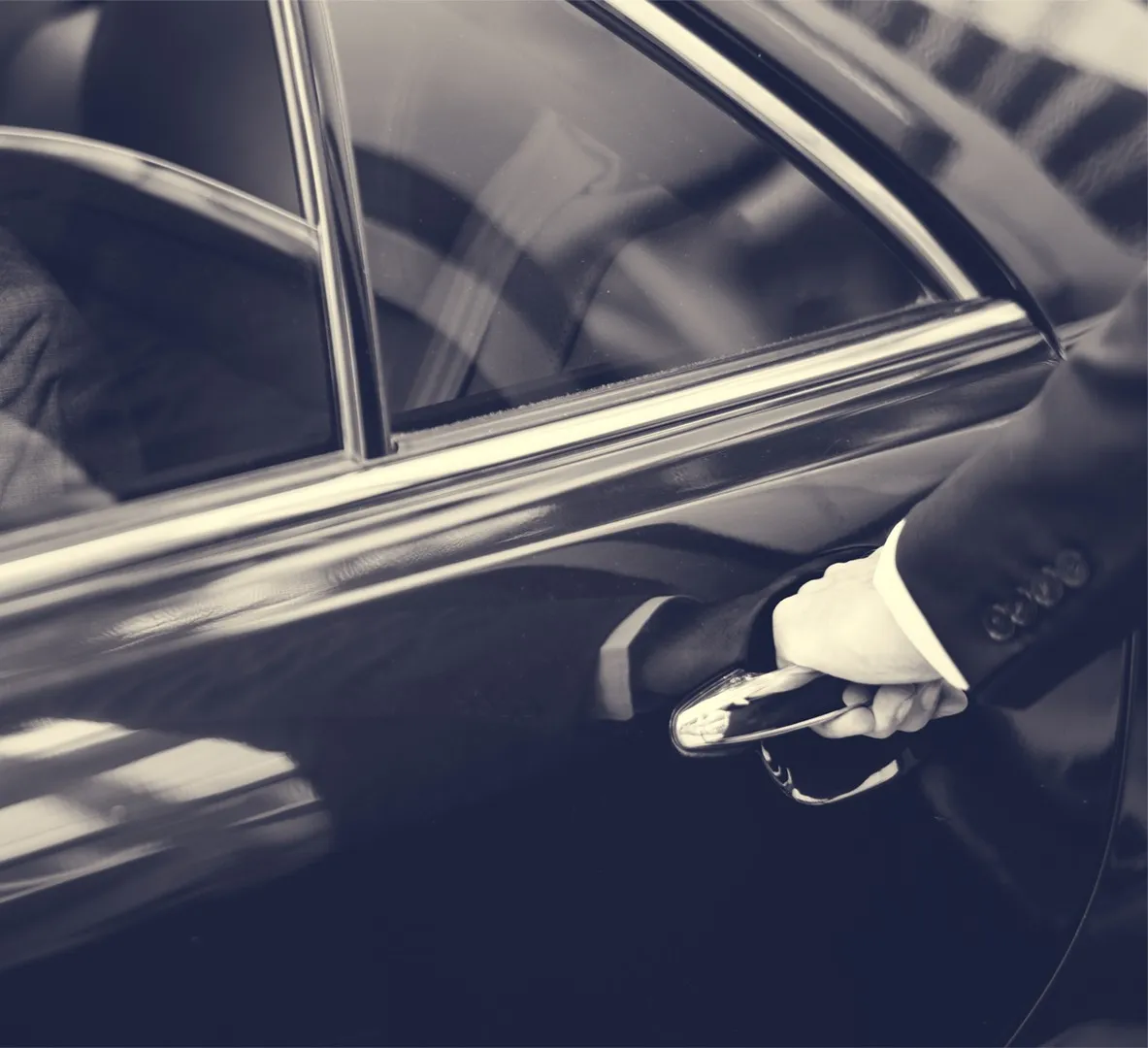 A suited hand on the chrome door handle of a black car