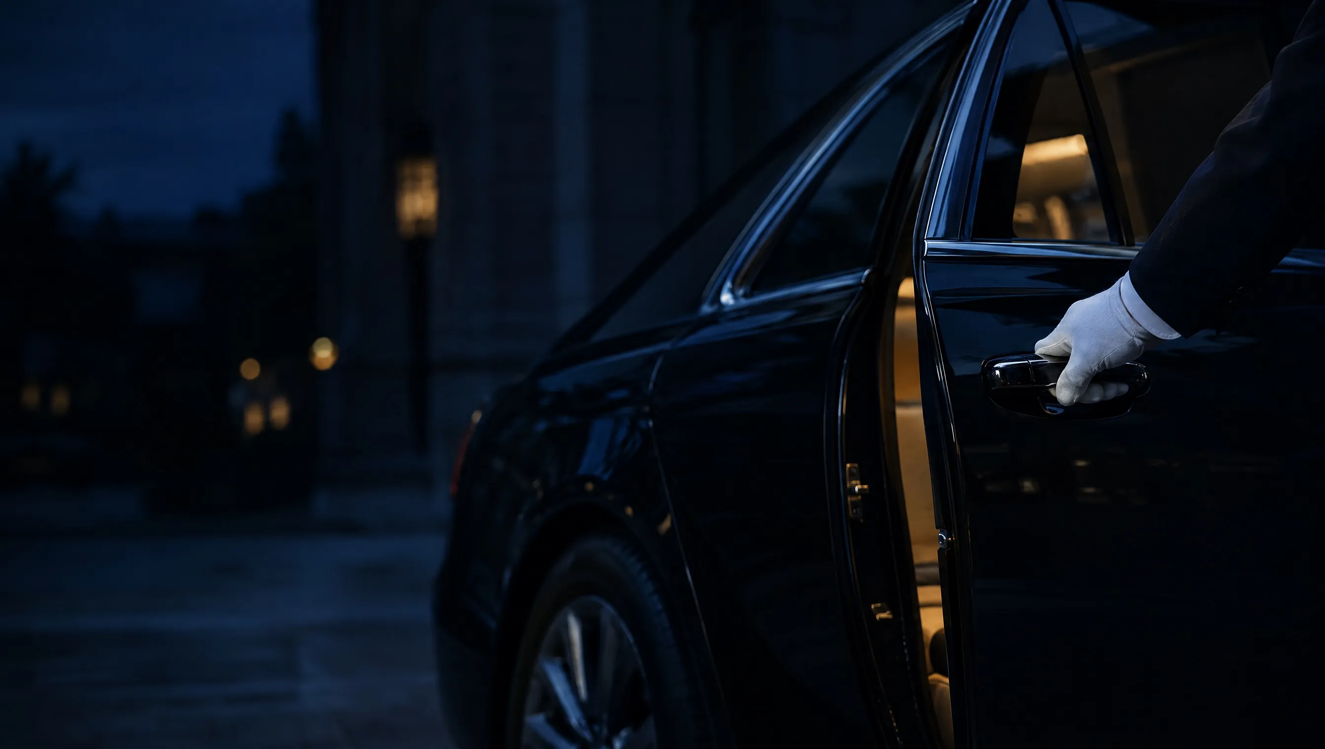 A white-gloved hand on the rear door handle of a black saloon at night, the door just opening onto a lit cabin